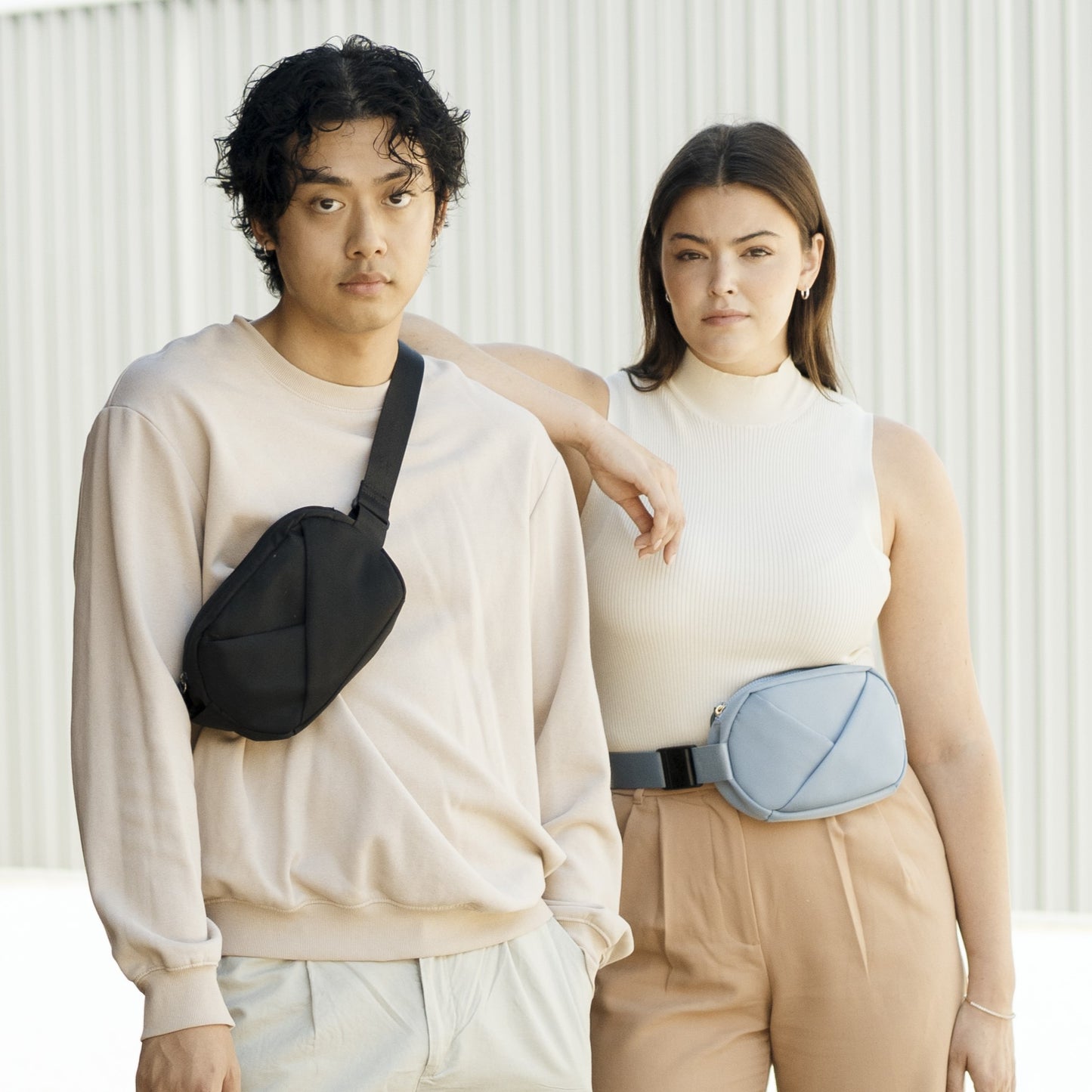 Lux & Nyx Origami Belt Bag and Sling Bag - Male Model Wearing The Black Belt Bag In Sling Bag Mode, and Female Model Wearing The Cashmere Blue Belt Bag In Belt Bag Mode