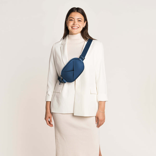 Woman wearing a white blazer and skirt with a navy blue crossbody bag on a light background