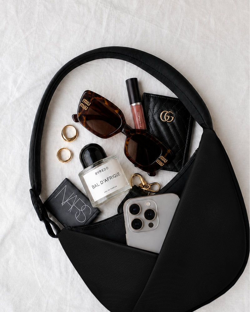 Black handbag with beauty products, sunglasses, and a phone on a white background
