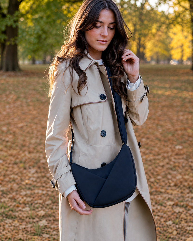 Woman in a beige trench coat holding a navy blue bag in an autumn park.