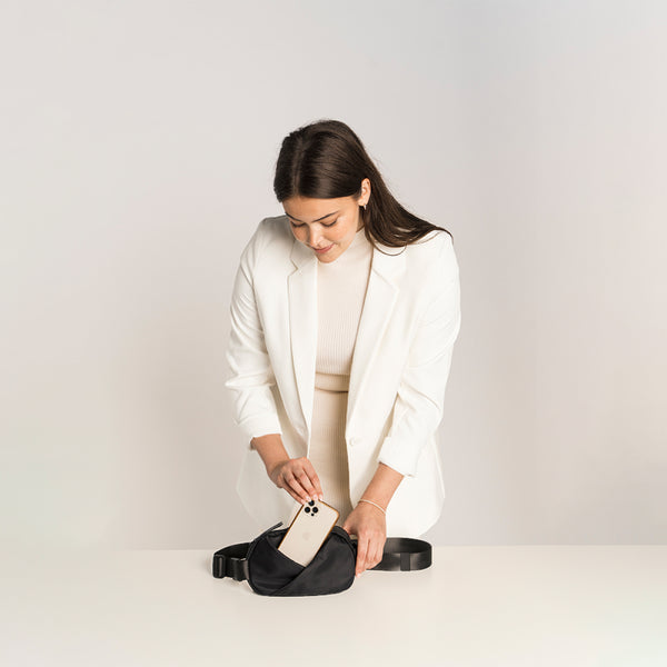 Woman in a white blazer interacting with a black waist bag .