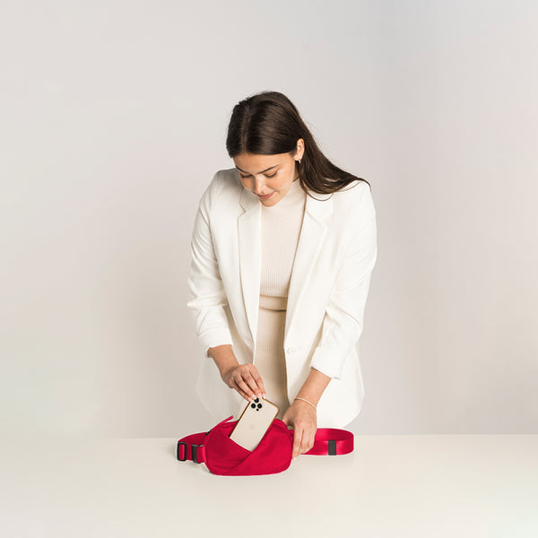 Woman holding a phone in a Cardinal Red waist bag.