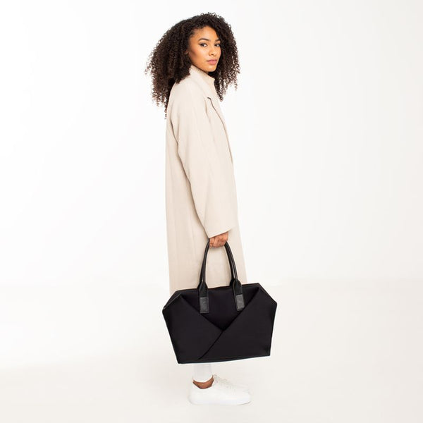 Woman holding a Lux & Nyx Large Origami Tote Ultra Matte - 15" Laptop Tote With Luggage Sleeve - Black + Gold Hardware 