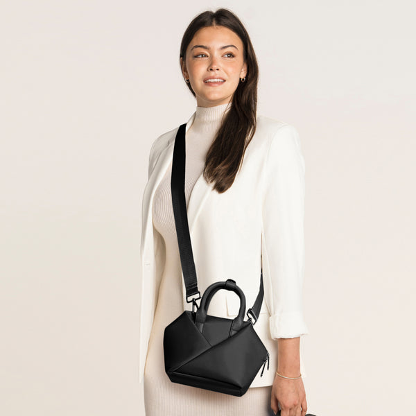 Woman holding a Black + Gold Hardware handbag against.