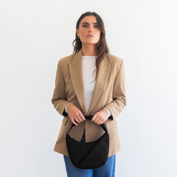 Woman wearing a beige blazer with a black bag on a white background