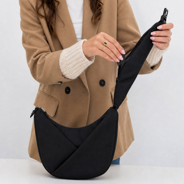 Person holding a black crossbody bag against a white background