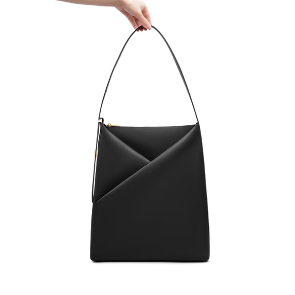 Black Origami Hobo Bag held by its handle, emphasizing the structured origami silhouette.

