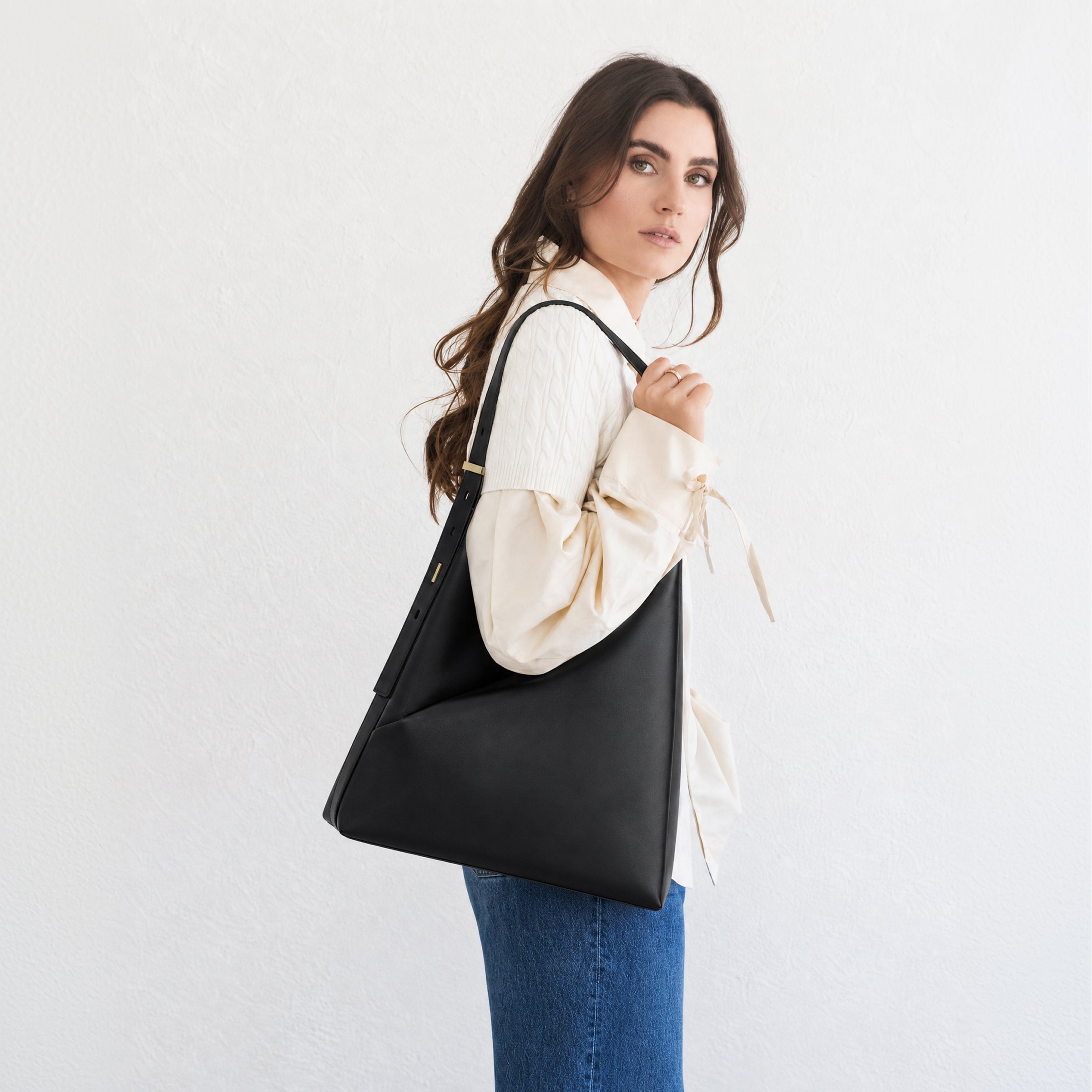 Model carrying the black Origami Hobo Bag over her shoulder in a three-quarter back view with a white blouse.
