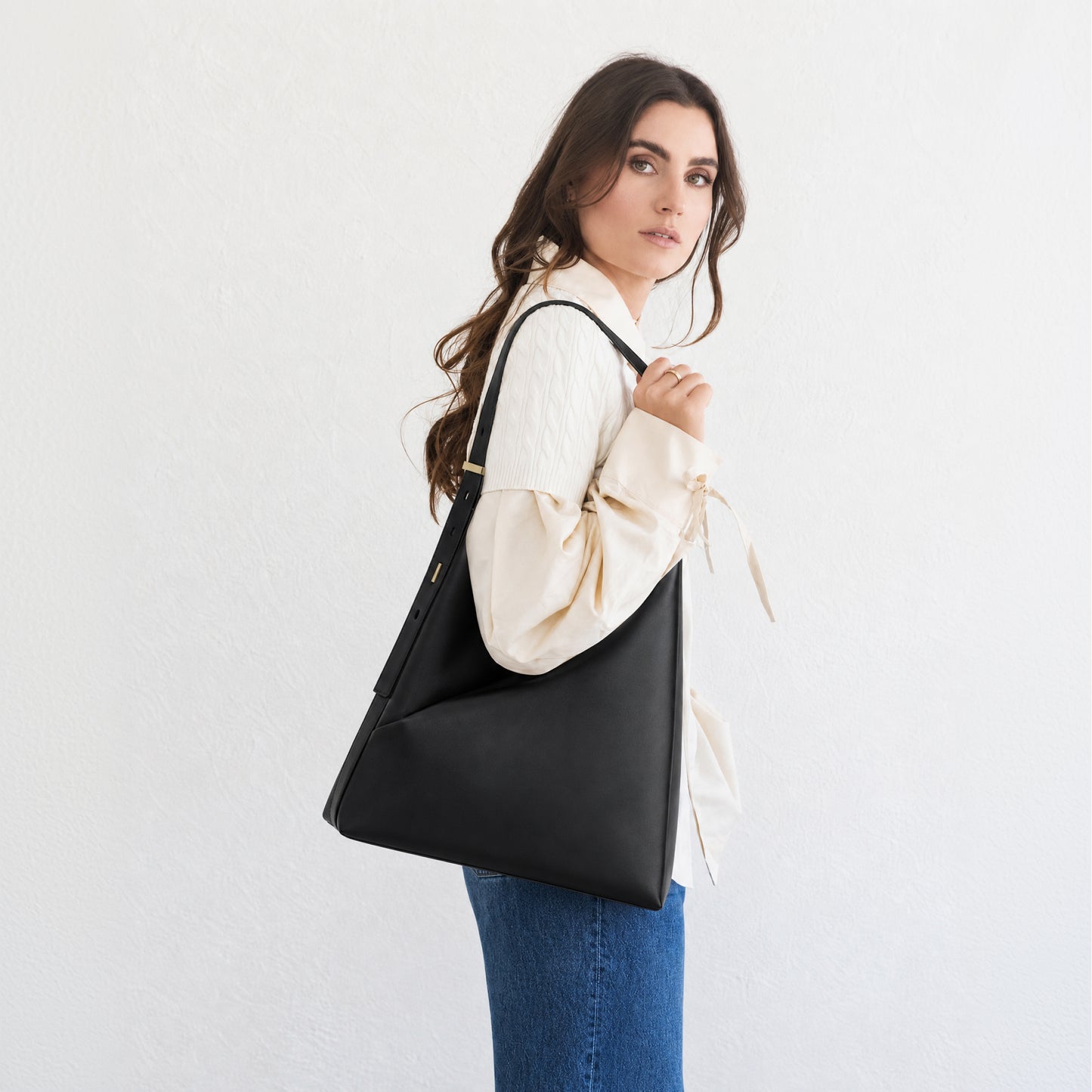 Model carrying the black Origami Hobo Bag over her shoulder in a three-quarter back view with a white blouse.