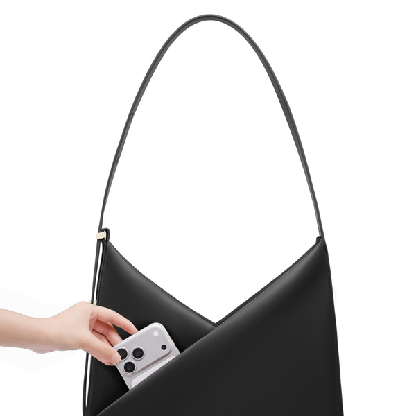 Hand placing a phone into the black Origami Hobo Bag to demonstrate its everyday capacity.
