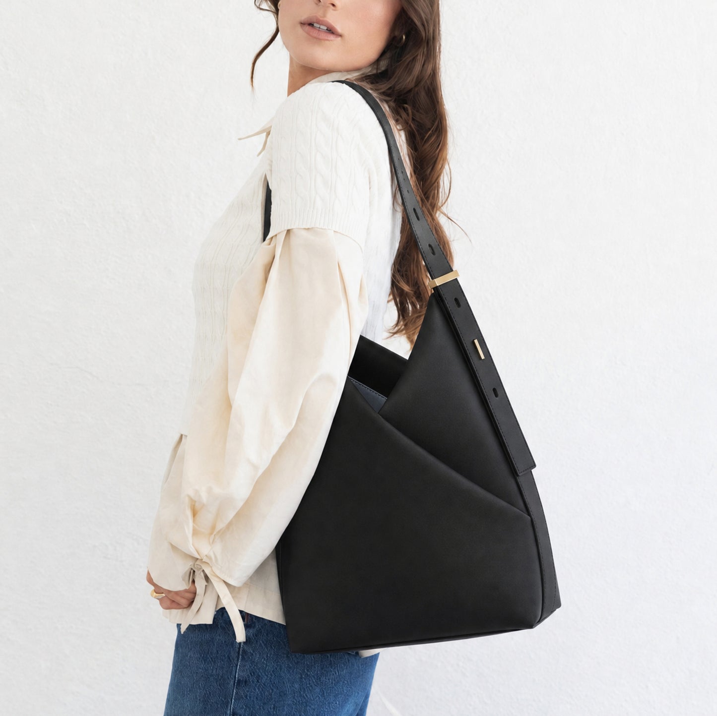 Model in a white blouse and jeans carrying the black Origami Hobo Bag over one shoulder.
