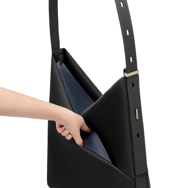Hand reaching into the open black Origami Hobo Bag, revealing the soft grey-blue interior lining and adjustable strap.
