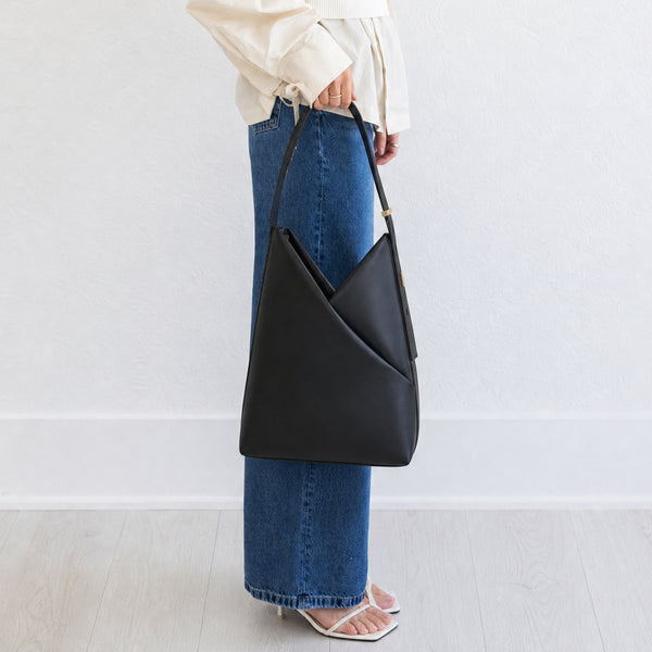 Model holding the black Origami Hobo Bag against her hip, styled with a white top and wide-leg jeans.
