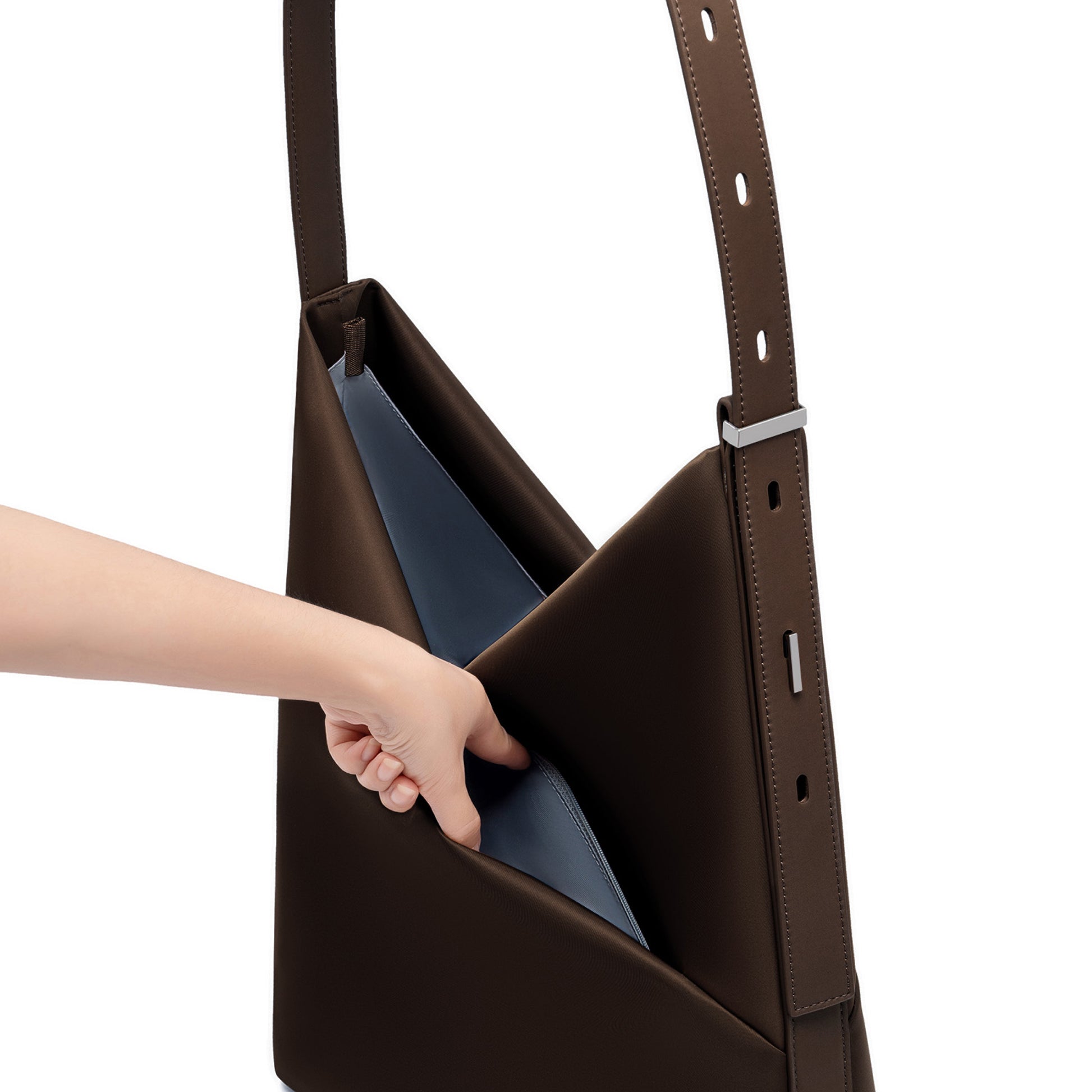 Hand reaching into the open espresso Origami Hobo Bag, revealing the soft grey-blue interior lining and adjustable strap.
