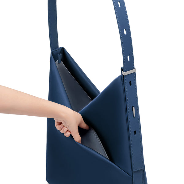 Hand reaching into the open navy Origami Hobo Bag, revealing the soft grey-blue interior lining and adjustable strap.
