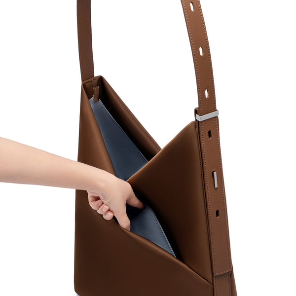 Hand reaching into the open sepia Origami Hobo Bag, revealing the soft grey-blue interior lining and adjustable strap.
