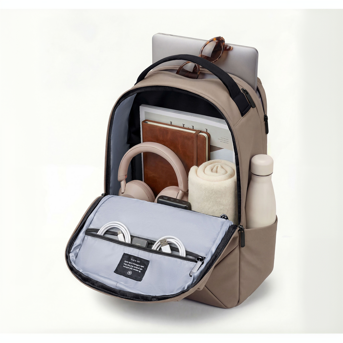 Lux & Nyx Origami Backpack - 16" Laptop Backpack With Trolley Strap - 
Champagne Taupe shown open on a clean white background, filled with travel accessories including a laptop, notebooks, headphones, a rolled sweater, earbuds, and a bottle in the side pocket.