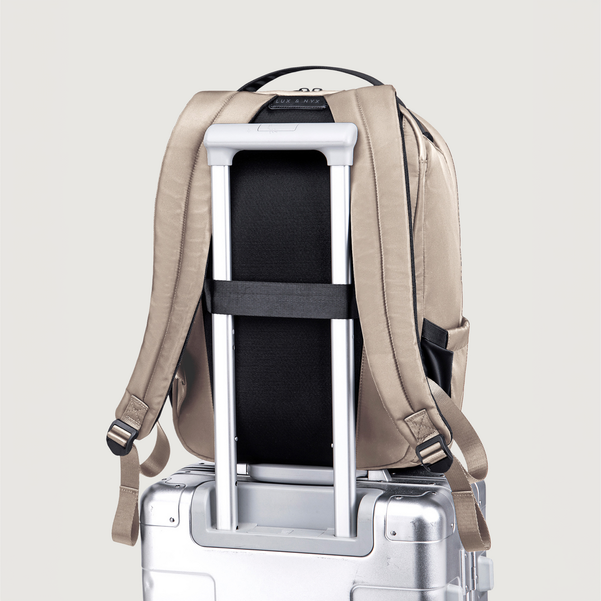 Lux & Nyx Origami Backpack - 16" Laptop Backpack With Trolley Strap - 
Champagne Taupe mounted on top of a silver rolling suitcase. 