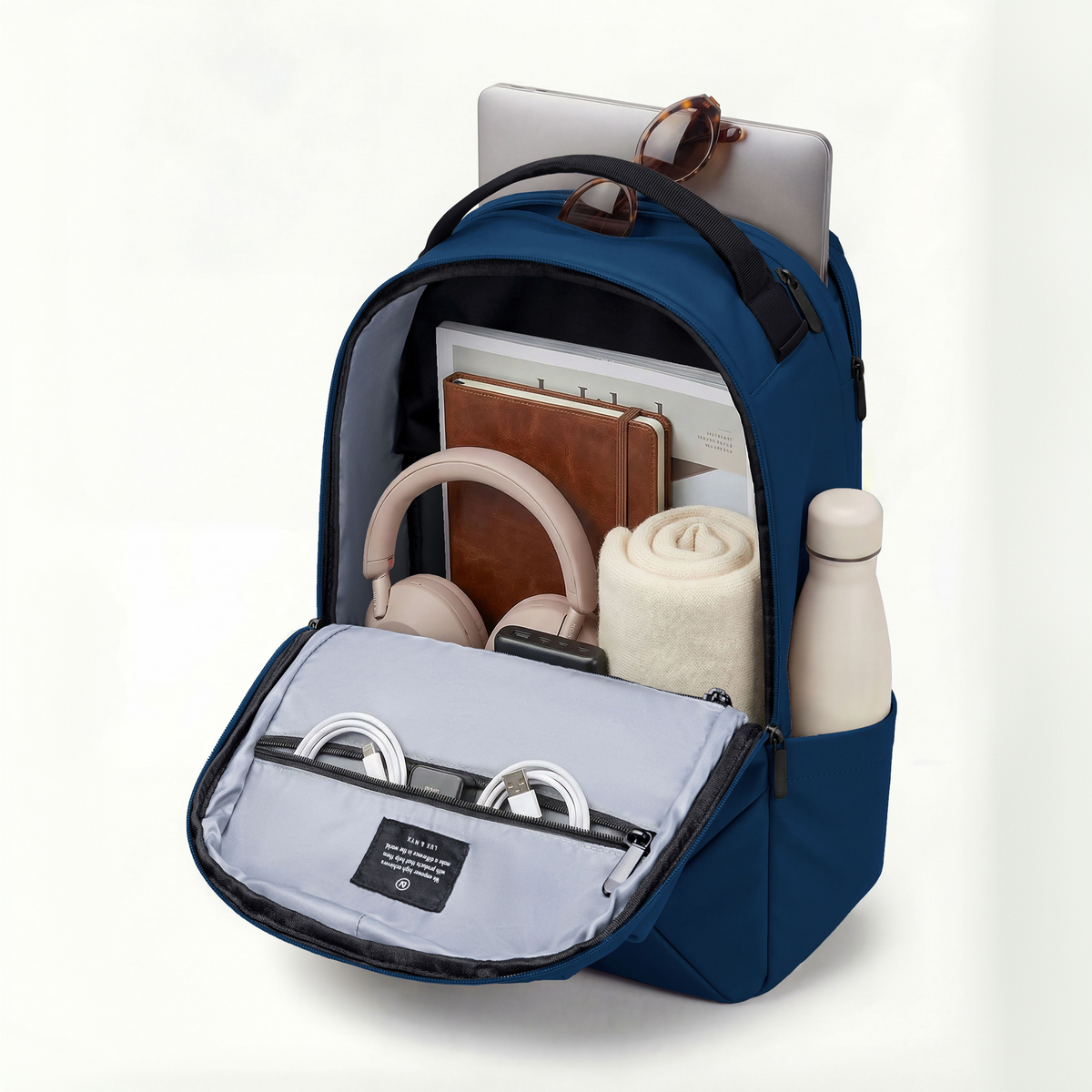 Lux & Nyx Origami Backpack - 16" Laptop Backpack With Trolley Strap - 
Navy filled with travel accessories including a laptop, headphones, notebooks, a rolled blanket, a bottle, and earphones, photographed on a clean white background.