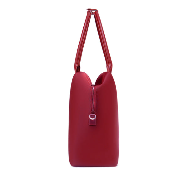 Side profile of a crimson red origami handbag highlighting its slim depth, arched top handles, and clasp closure.
