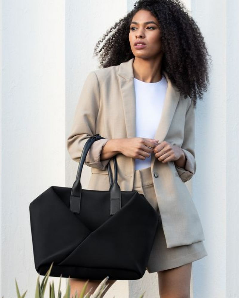 Woman holding a black tote bag against a light background
