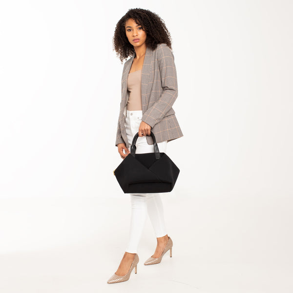 Side view of a woman carrying the Mid Origami handbag by hand. Available in black with silver hardware