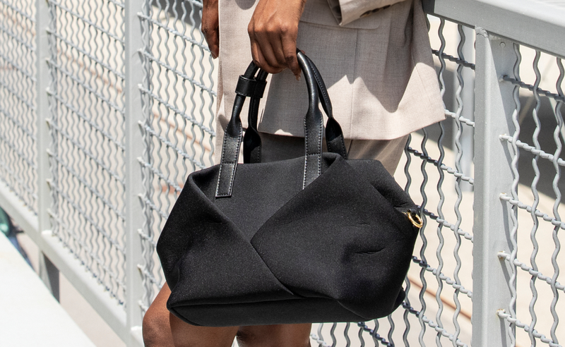 Person holding a black handbag against a metallic fence background
