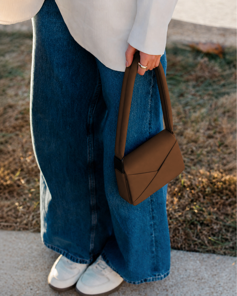 Person wearing blue jeans and a white top, holding a brown handbag outdoors.