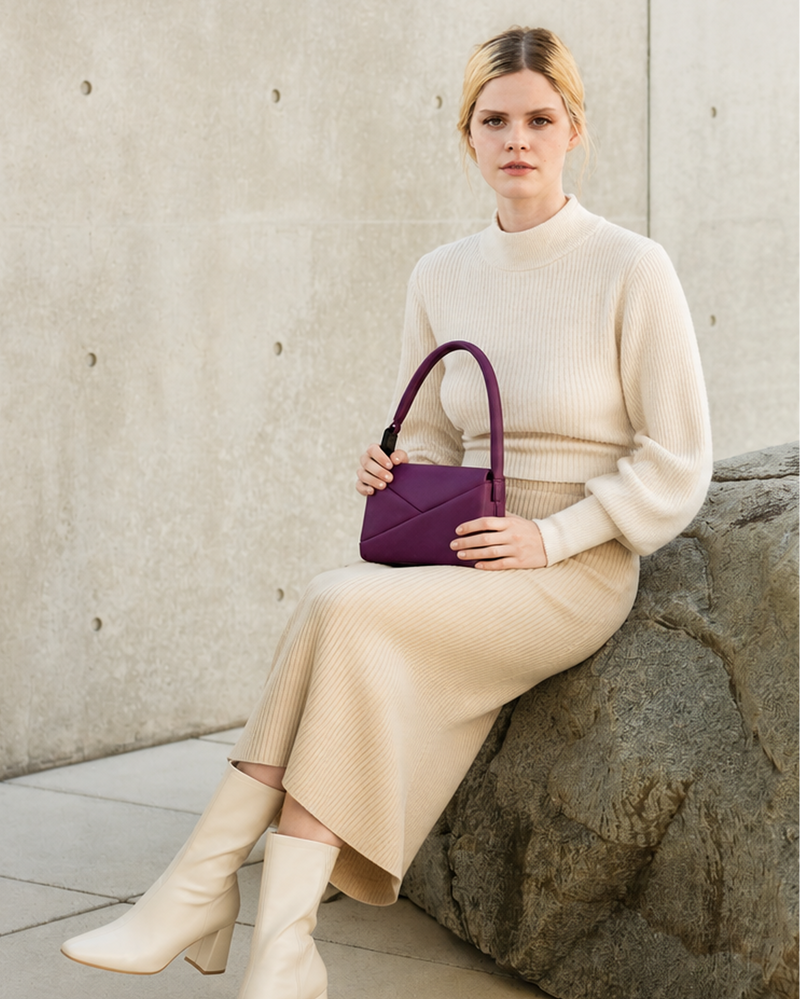 Woman holding a purple handbag against a concrete wall.