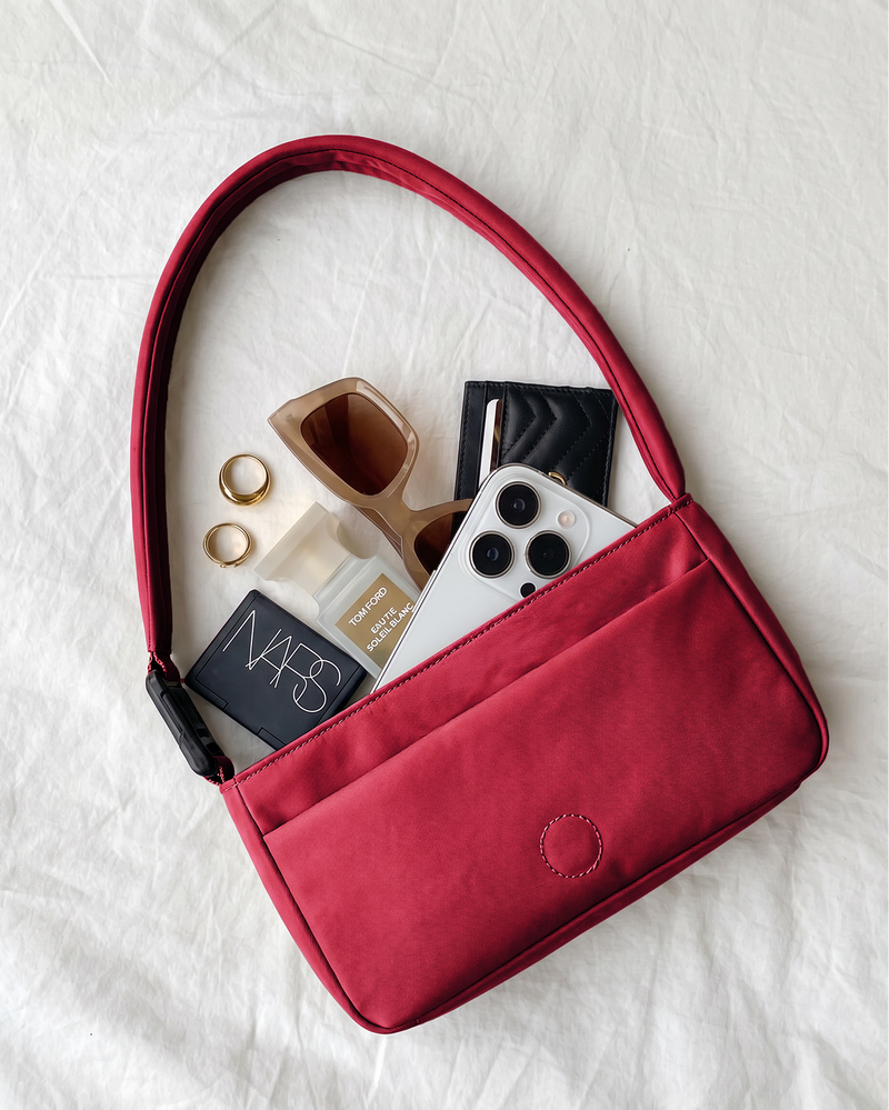Red crossbody bag with phone, makeup items, and a bottle on a white background