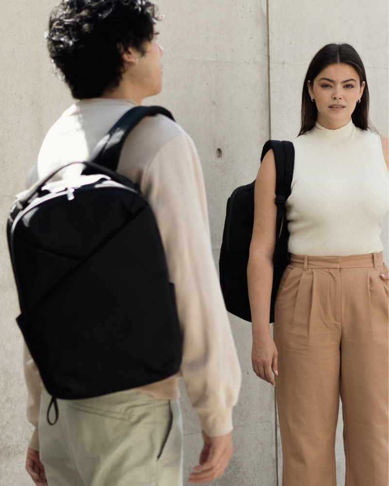Two people wearing black backpacks against a plain background