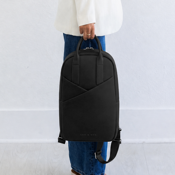 Woman carrying Origami Slim Black Backpack by top handle at side, casual handheld carry style