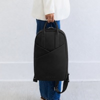 Woman carrying Origami Slim Backpack by top handle at side, casual handheld carry style