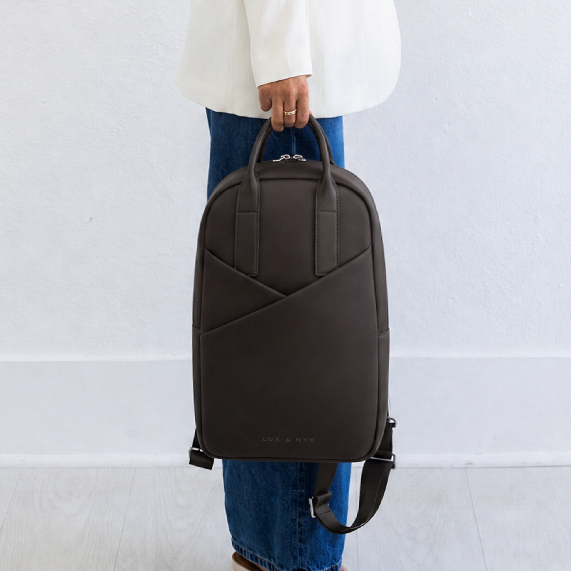 Woman carrying Origami Slim Espresso Backpack by top handle at side, casual handheld carry style