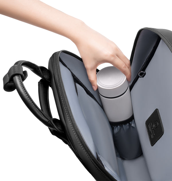 Hand placing a reusable water bottle into the dedicated interior bottle pocket of a black backpack, showcasing organized storage and easy access inside the spacious main compartment.