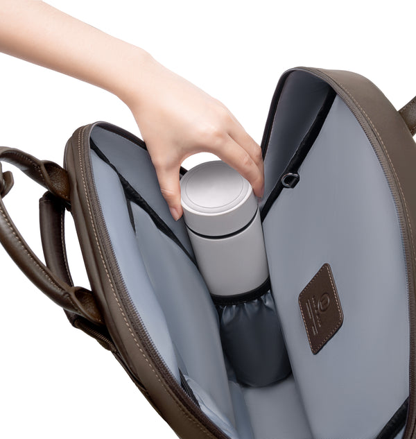Hand placing a reusable water bottle into the dedicated interior bottle pocket of an espresso backpack, showcasing organized storage and easy access inside the spacious main compartment.