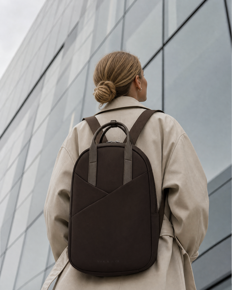 Person wearing a brown backpack against a modern building.