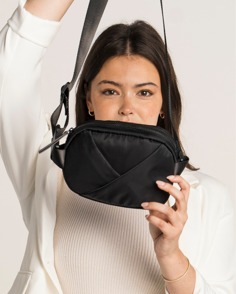 Person holding a black origami belt bag in front of their face on a white background