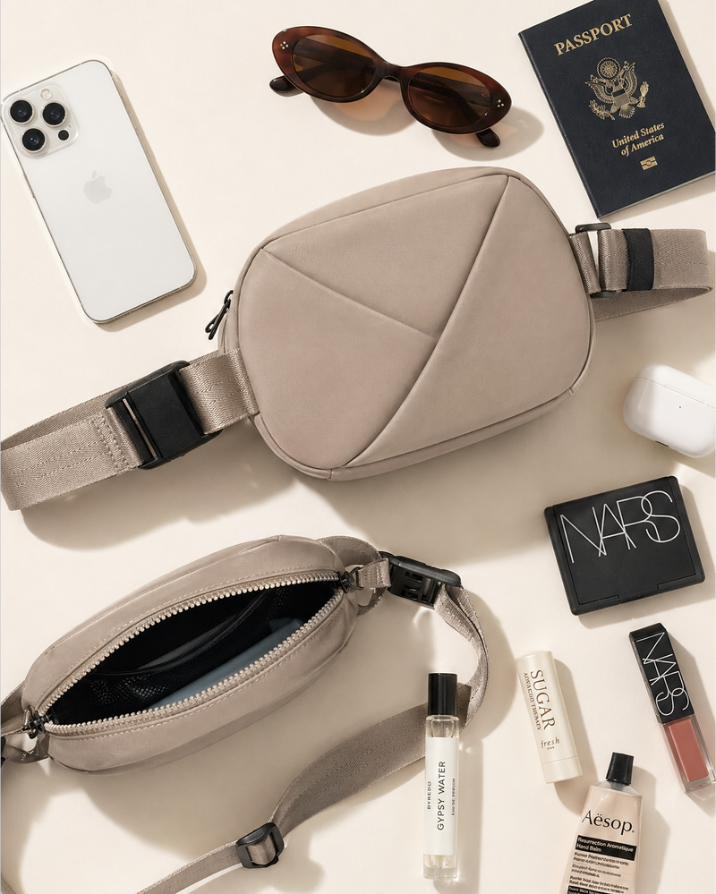 Beige crossbody bag with phone, sunglasses, passport, and beauty products on a light background