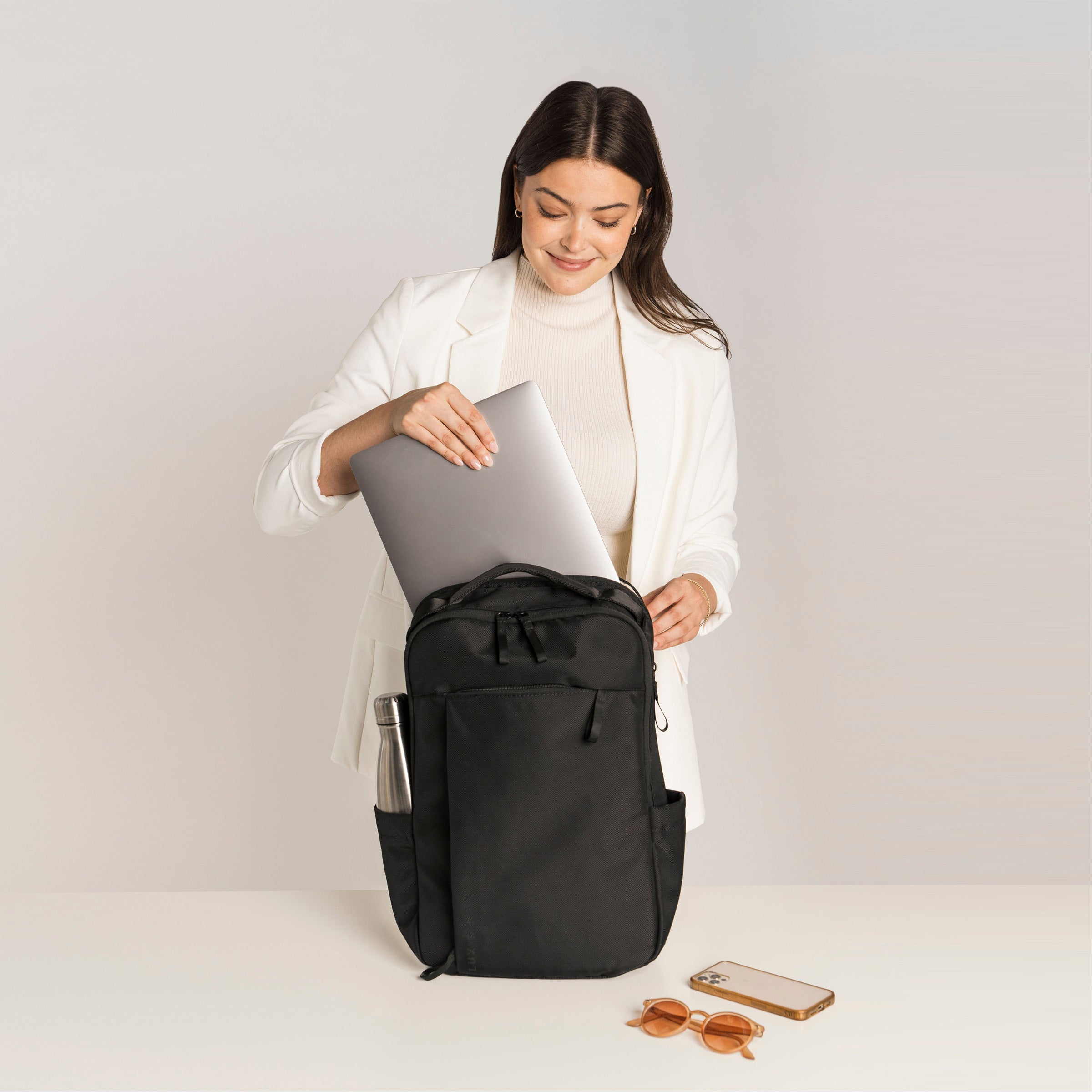 Lux & Nyx Purpose Backpack - 16" Laptop Backpack With Trolley Strap - Black - Professional Woman Putting A 16” Laptop Backpack in The 16” Padded Laptop Compartmentt
