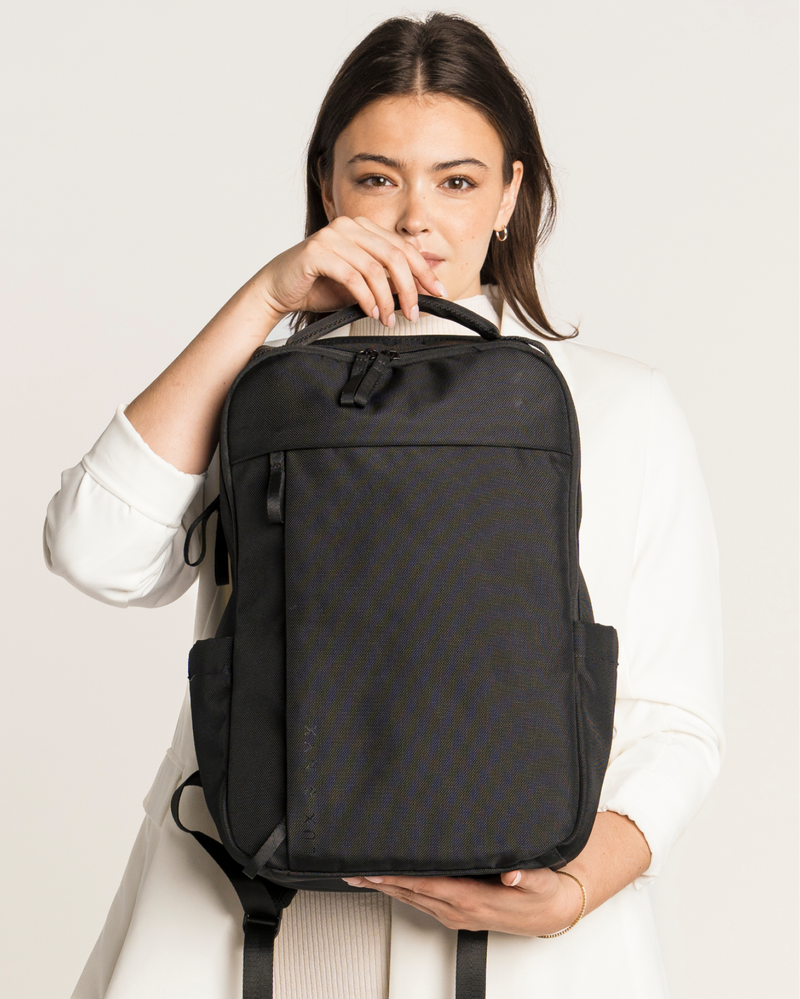 Woman holding a black backpack against a plain background