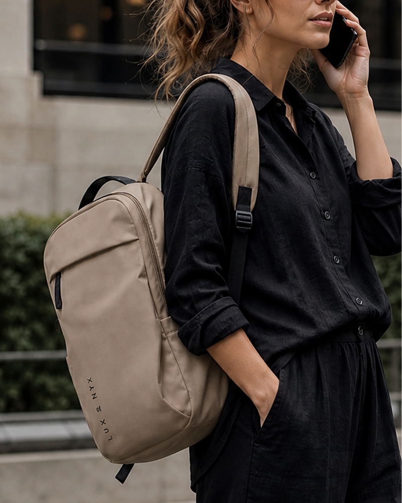 Person wearing a beige backpack and black shirt, talking on a phone outdoors.