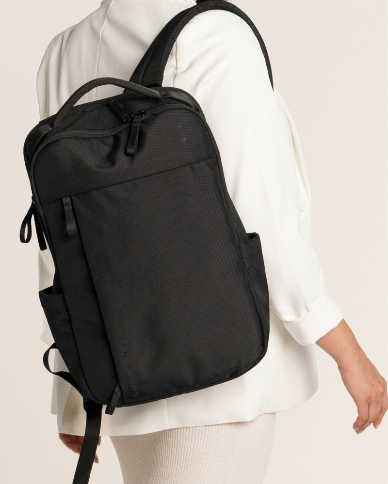 Black backpack worn by a person on a plain background