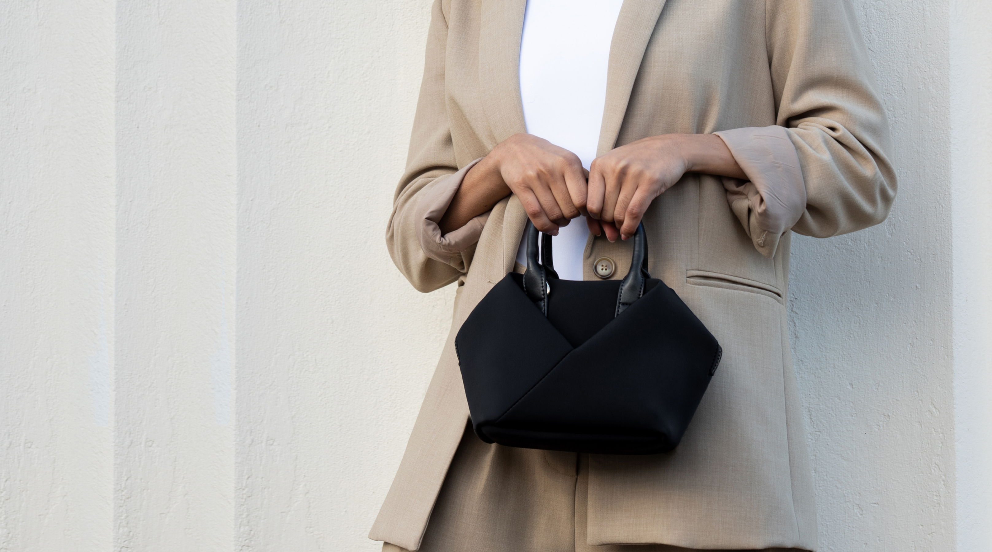 Person holding a black handbag against a plain background