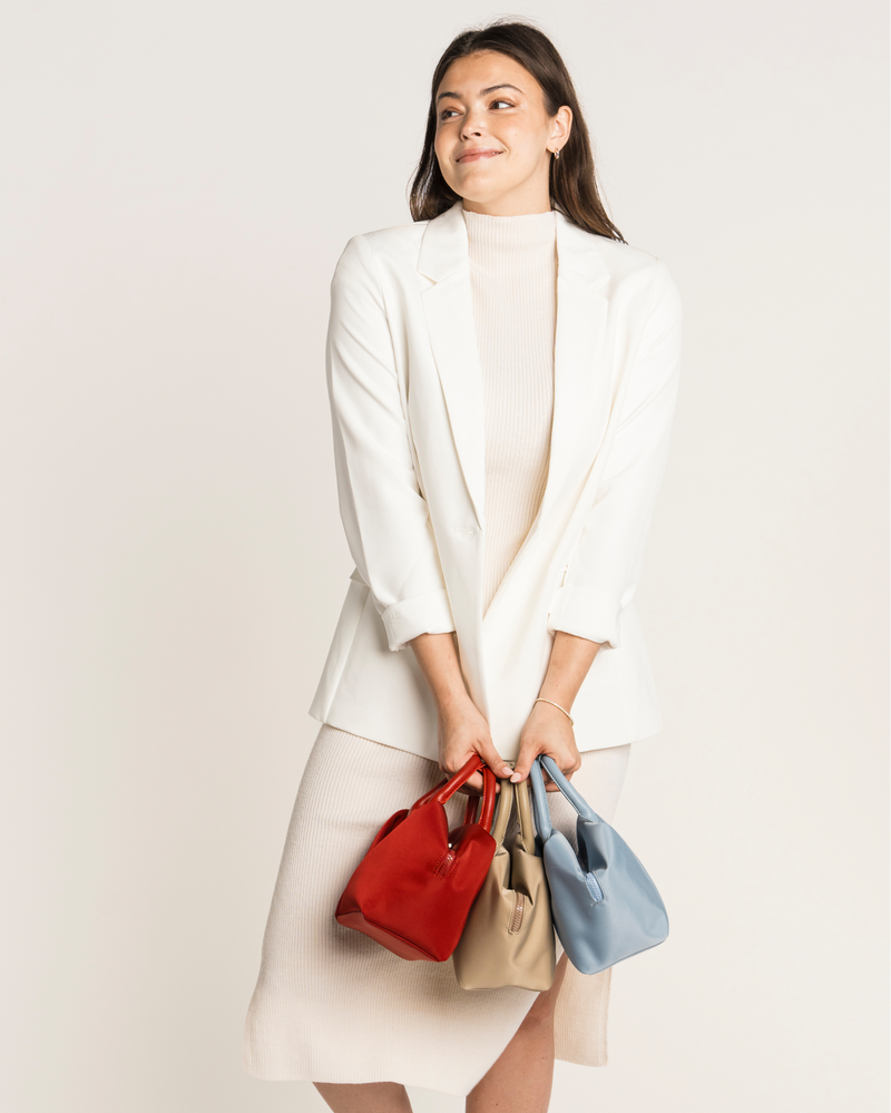 Woman holding three handbags against a plain background