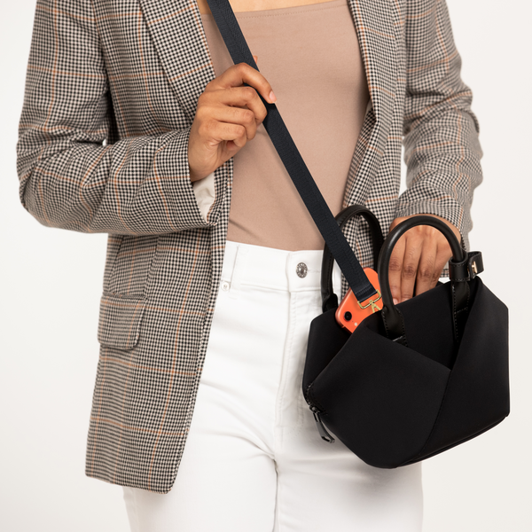 Person wearing a black-with-gold-hardware crossbody handbag with gold-tone hardware, featuring a visible smartphone inside the bag.